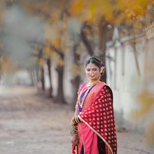 Young woman in vibrant saree posing outdoors with fall foliage.