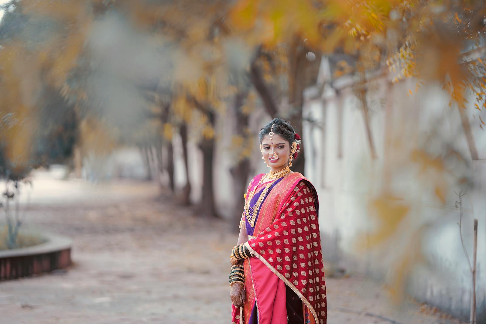 Young woman in vibrant saree posing outdoors with fall foliage.