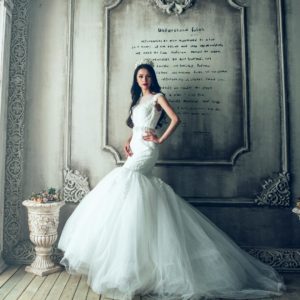 Stunning bride in elegant wedding dress posing in ornate, vintage interior.