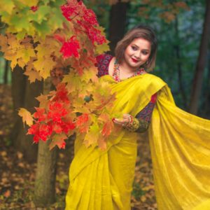 Portrait of a woman in a yellow saree holding bright autumn leaves in a serene forest.