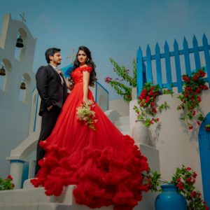 Couple posing together in vibrant red gown with blue accents, outdoors.